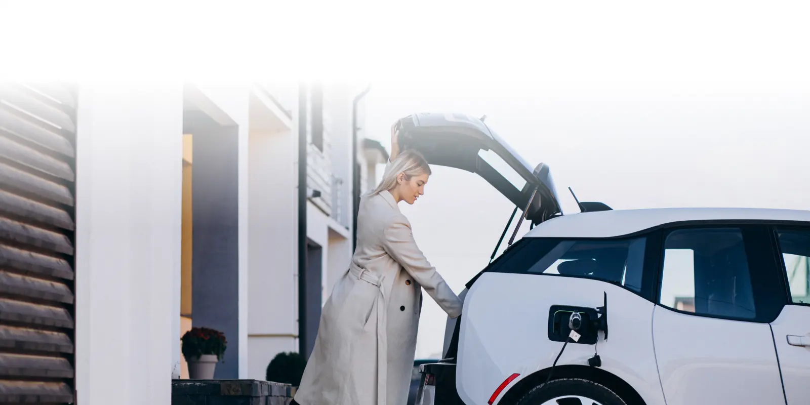 Nő pakol egy töltés alatt álló fehér elektromos autó csomagtartójába