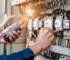 Villanyszerelő lakatfogós műszerrel méri az elektromos hálózat terhelhetőségét a töltő telepítése előtt