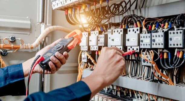 Villanyszerelő lakatfogós műszerrel méri az elektromos hálózat terhelhetőségét a töltő telepítése előtt